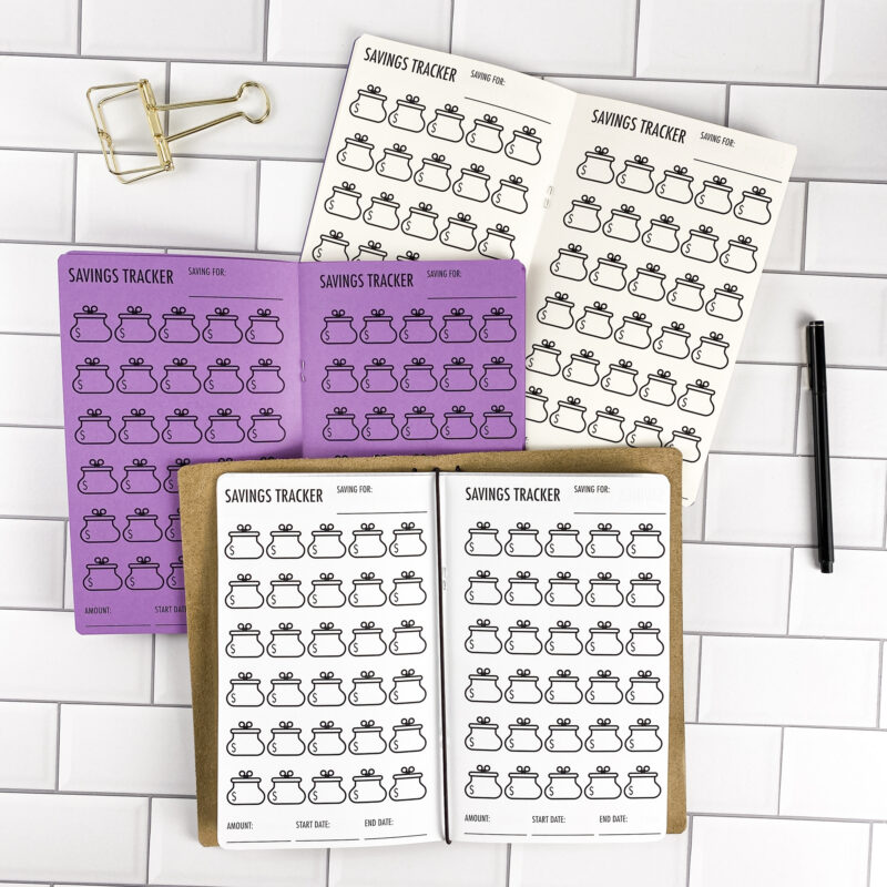 Savings Tracker Purse traveler's notebook refill by CityGirl Planners, showing savings tracker pages with a purse illustration design. Three booklets displayed in different paper color options inside a traveler's notebook cover.