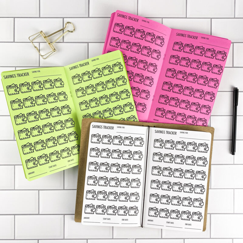 Savings Tracker Wallets traveler's notebook refill by CityGirl Planners, showing savings tracker pages with a wallet illustration design. Three booklets displayed in different paper color options inside a traveler's notebook cover.