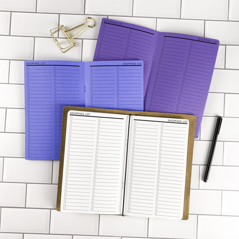 Shopping List traveler's notebook refill by CityGirl Planners, showing shopping list pages for organizing grocery and errand lists. Three booklets displayed in different paper color options inside a traveler's notebook cover.