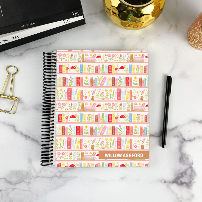 7x9 spiral bound planner in the Storybook Shelf cover design on a marble surface with styling accessories.
