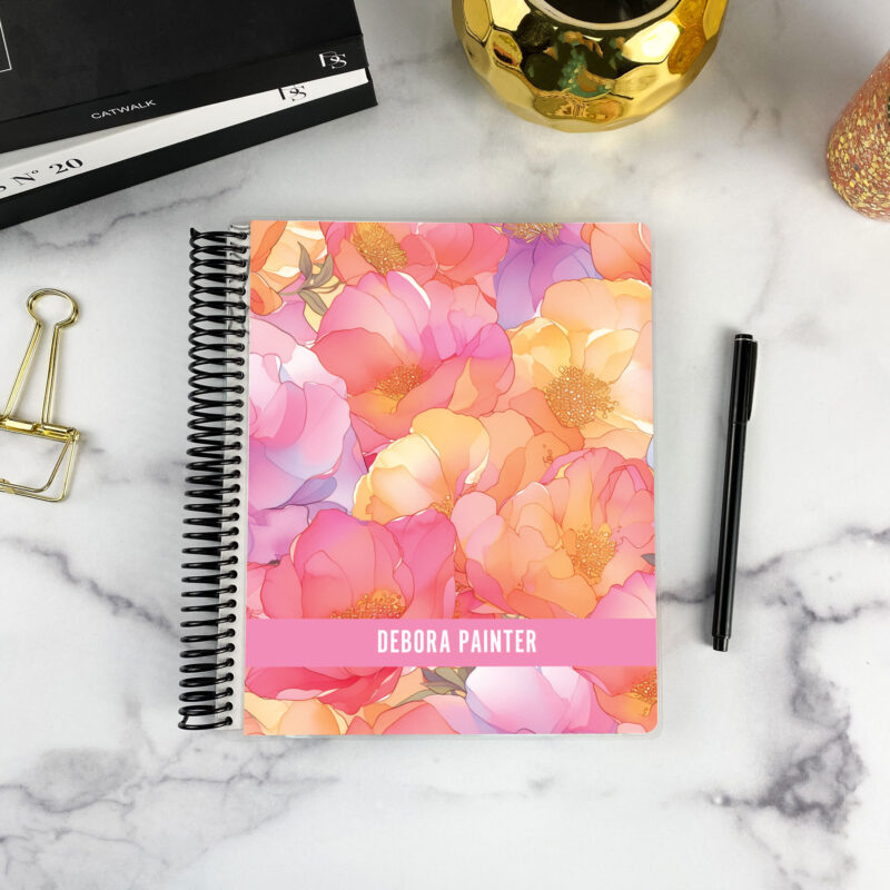 7x9 spiral bound planner in the Sunset Blooms cover design on a marble surface with styling accessories.