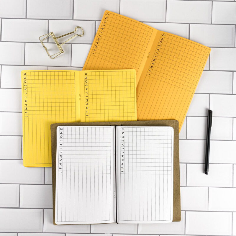 Task Tracker traveler's notebook refill by CityGirl Planners, showing task tracker pages for managing to-do items and priorities. Three booklets displayed in different paper color options inside a traveler's notebook cover.