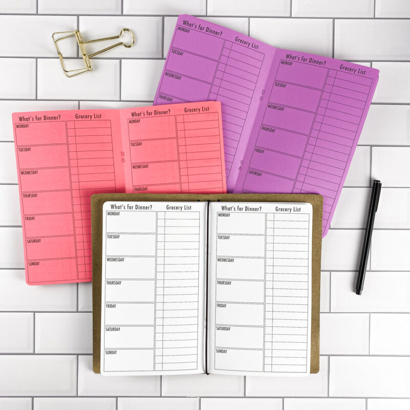 What's for Dinner traveler's notebook refill by CityGirl Planners, showing weekly meal planning pages for organizing dinner plans. Three booklets displayed in different paper color options inside a traveler's notebook cover.