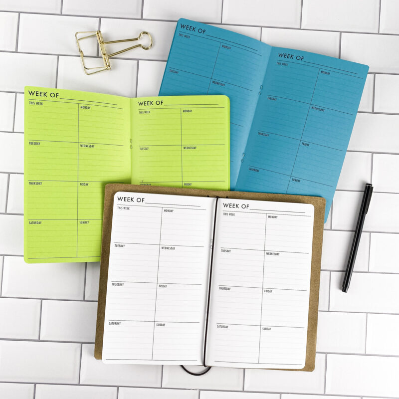 Week on 1 Page Vertical traveler's notebook refill by CityGirl Planners, showing vertical weekly planner layout fitting a full week on one page. Three booklets displayed in different paper color options inside a traveler's notebook cover.